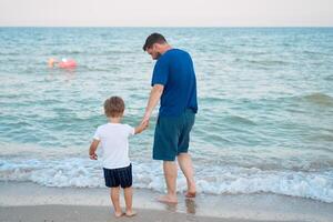pai filho gastos Tempo juntos mar período de férias jovem Papai criança pequeno Garoto caminhando de praia foto