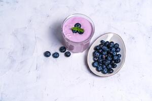saboroso fresco mirtilo iogurte mexe sobremesa dentro vidro em pé em branco mesa fundo. foto