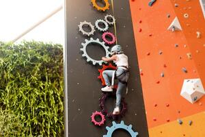 criança escalada em parede dentro diversão Centro. escalada Treinamento para crianças. pequeno menina dentro vestido escalada engrenagem escalar alto. extremo ativo lazer para crianças. foto