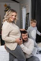 feliz família conceito. marido abraço barriga grávida esposa em pé interior vivo quarto perto sofá foto