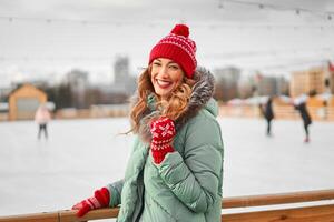 lindo adorável meia idade menina com encaracolado cabelo caloroso inverno jaquetas carrinhos gelo rinque fundo Cidade quadrado. foto