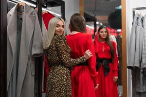 dois mulheres amigas dentro uma moda boutique escolher uma casaco para outono temporada. foto