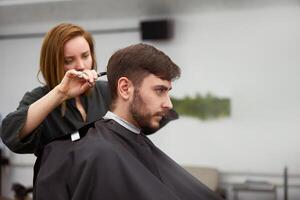 bonito azul olhos homem sentado dentro barbeiro fazer compras. estilista de cabelo cabeleireiro mulher corte dele cabelo. fêmea barbeiro. foto