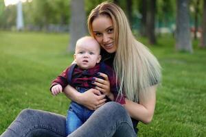 lindo jovem mãe anda em com dela pequeno filho dentro uma verão parque foto