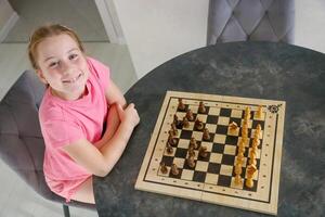 pequeno alegre menina às a mesa jogando xadrez foto