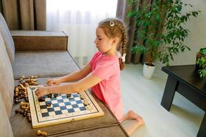 pequeno menina às casa jogando com jogo de damas e xadrez peças foto