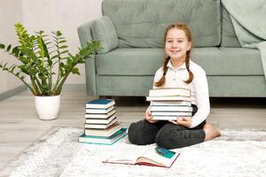 alegre pequeno menina às casa em a chão com livros dentro dela mãos foto