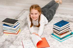 rindo menina às casa em a chão cercado de livros foto