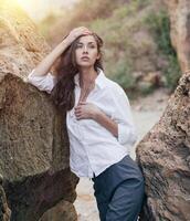 o negócio mulher em terno e branco camisa em pé perto grande pedra em a mar custo foto