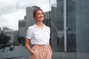 empresária bem sucedido mulher o negócio pessoa em pé ao ar livre corporativo construção exterior. sorrir feliz caucasiano confiança profissional o negócio mulher meio era foto