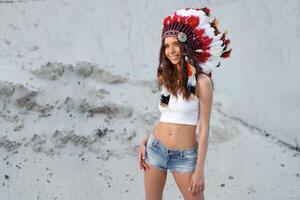 uma lindo jovem caucasiano menina dentro uma branco topo e jeans calção em dela cabeça é vestindo a indiano chapéu. barata é dentro a deserto. feliz feriado humor. foto