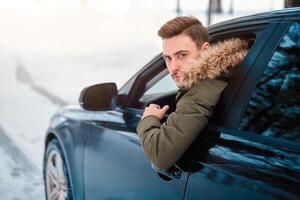 jovem atraente caucasiano homem senta às a roda do dele carro ensolarado inverno dia. foto