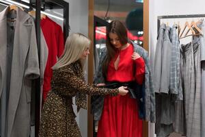 dois mulheres amigas dentro uma moda boutique escolher uma casaco para outono temporada. foto