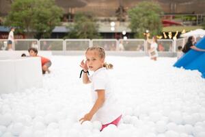 feliz pequeno menina jogando branco plástico bolas piscina dentro diversão parque. Parque infantil para crianças. foto
