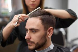 bonito azul olhos homem sentado dentro barbeiro fazer compras. estilista de cabelo cabeleireiro mulher corte dele cabelo. fêmea barbeiro. foto