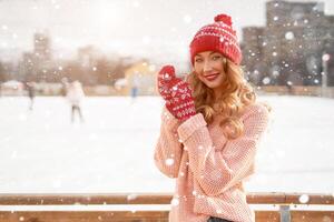 lindo adorável meia idade menina com encaracolado cabelo caloroso inverno suéter carrinhos gelo rinque fundo Cidade quadrado. foto