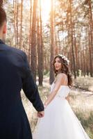 Segue mim meu amor conceito. atraente jovem mulher vestido dentro branco Casamento vestir segurando mão do dela namorado e caminhando em a lindo jardim para feliz futuro foto
