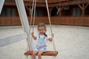 brincalhão criança oscilante balanço. alegre pequeno menina jogar tendo Diversão Parque infantil horário de verão foto