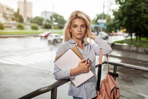 entusiasmado sério lindo jovem menina segurando pilha do livros em pé perto campus estilo de vida positividade acadêmico graduando universidade escola foto