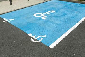 internacional deficiente símbolo pintado dentro brilhante azul em uma compras Centro estacionamento espaço. a espaço é claramente marcado em qualquer lado com adicional branco diagonal listras. foto