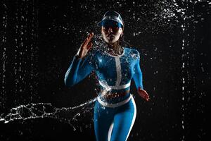 lindo jovem menina dentro ultramar azul pássaro cor roupa de esporte correndo dentro aqua estúdio. gotas do água espalhar sobre dela ginástica corpo em a fundo do água salpicos. foto