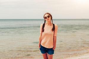 uma hipster menina com trançado cabelo dentro tranças é caminhando ao longo a de praia dentro roupas. verão conceito, lazer turismo foto