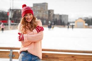 lindo adorável meia idade menina com encaracolado cabelo caloroso inverno suéter carrinhos gelo rinque fundo Cidade quadrado. foto