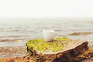 copo do café em a mar água e pedra fundo. mar frescor manhã conceito foto
