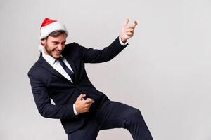 jovem bonito caucasiano cara dentro o negócio terno e santa chapéus carrinhos em branco fundo dentro estúdio e tocam em a imaginário guitarra. foto