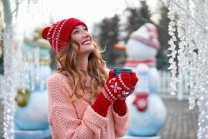 lindo adorável meia idade menina com encaracolado cabelo caloroso inverno suéter carrinhos fundo Cidade quadrado. foto