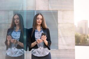 o negócio mulher 35 anos vestido listra camisa e Preto Jaqueta com grandes cabelo em pé perto escritório construção ao ar livre usar Smartphone foto