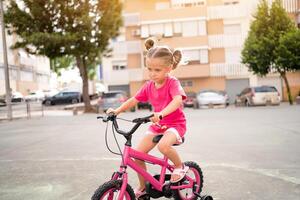 fofa pequeno sorridente menina equitação bicicleta bicicleta dentro cidade em estacionamento ensolarado verão dia. ativo família lazer com crianças. foto