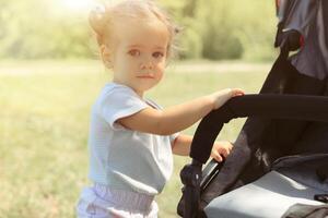 bebê menina em pé perto uma bebê transporte foto