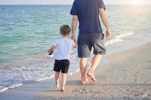 pai filho gastos Tempo juntos mar período de férias jovem Papai criança pequeno Garoto caminhando de praia foto