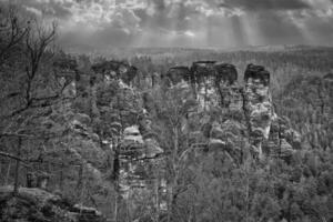 irregular pedras às a Basteibridge. Largo Visão sobre árvores e montanhas. dramático céu foto