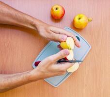 fechar acima masculino mãos cortar a maçã para dentro fatias. topo Visão do preparando frutas sobre cozinha mesa. foto