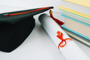 uma Preto quadrado graduado chapéu com uma vermelho pendão mentiras em uma diploma e uma pilha do livros. Educação conceito foto