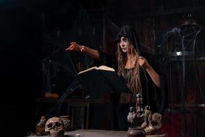 dia das Bruxas conceito. bruxa vestido Preto de capuz com tranças em pé Sombrio masmorra quarto usar Magia livro para conjuração Magia soletrar foto