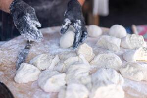 chefe de cozinha dentro Preto luvas cortes cru massa para dentro peças faço pizza hambúrgueres pão. foto