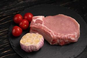 topo Visão do 1 peças cru carne de porco Picar bifes com cereja tomates e alho em uma Preto pedra corte borda. foto