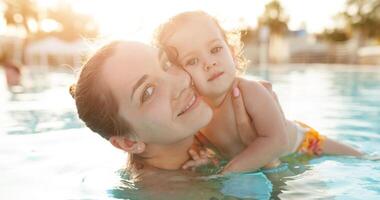 mãe e pequeno filha estão reproduziu dentro a aberto natação piscina. família com 1 criança em período de férias dentro caloroso países. positivo pessoas em período de férias. foto