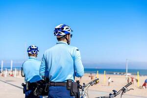 dois policial patrulhando beira-mar passeio em bicicletas. pessoas estão queimadura de sol em a cidade público de praia em a atlântico costa. foto