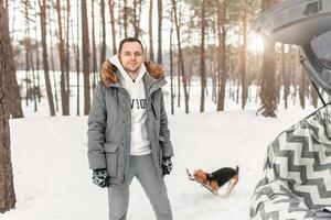 uma jovem homem vestido dentro uma cinzento inverno parque dentro uma Nevado inverno floresta com beagle. conceito sobre inverno lazer e amor para animais foto