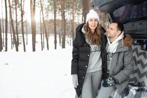 uma jovem família do Viajantes cara e menina estão sentado dentro a tronco do dele carro dentro a abraçar. uma andar do uma jovem casal dentro a inverno pinho floresta. amor foto