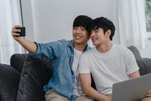 selfie engraçado jovem casal gay romântico pelo celular em casa. Amante asiático masculino feliz relaxa a diversão usando tecnologia de telefone móvel sorrindo tirar uma foto juntos enquanto estava deitado sofá no conceito de sala de estar.