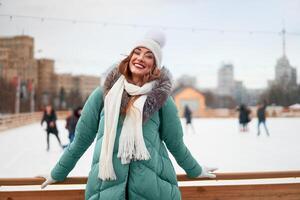 lindo adorável meia idade menina com encaracolado cabelo caloroso inverno jaquetas carrinhos gelo rinque fundo Cidade quadrado. foto