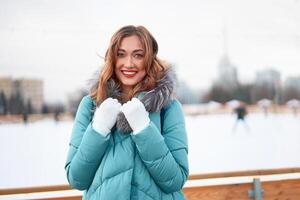 lindo adorável meia idade menina com encaracolado cabelo caloroso inverno jaquetas carrinhos gelo rinque fundo Cidade quadrado. foto