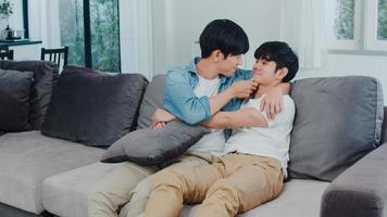 jovem casal gay asiático abraço e beijo em casa. atraentes asiáticos lgbtq orgulho homens felizes relaxam passam um tempo romântico juntos enquanto estava deitado sofá no conceito de sala de estar. foto