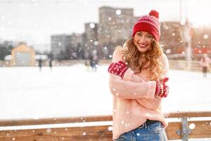 lindo adorável meia idade menina com encaracolado cabelo caloroso inverno suéter carrinhos gelo rinque fundo Cidade quadrado. foto