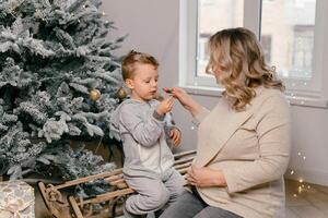 feriado Natal caucasiano mãe jogando com pequeno fofa filho perto decorado Novo ano árvore às casa foto